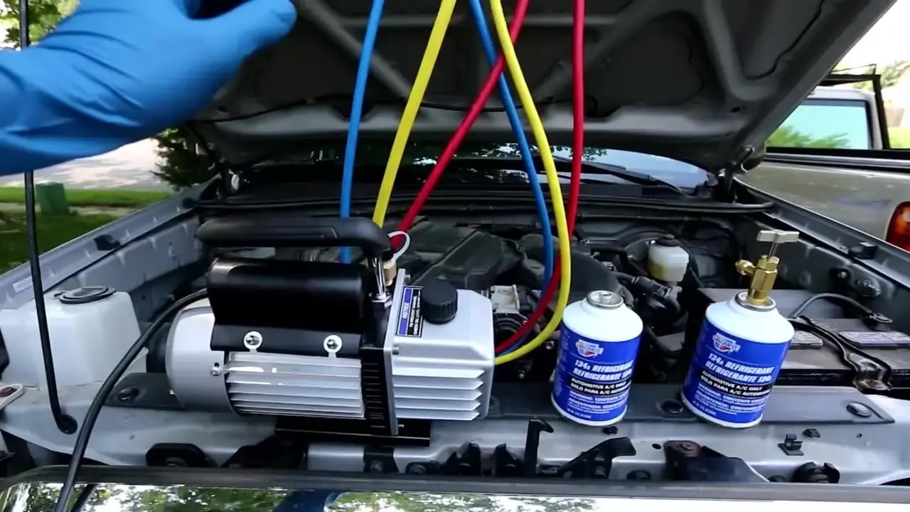 Close-up of a car engine bay with professional pressure gauges and gas canisters connected to the air conditioning system.