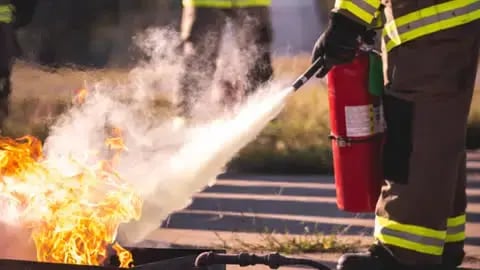 A firefighter using a fire extinguisher to suppress a controlled fire, demonstrating safety and compliance training.