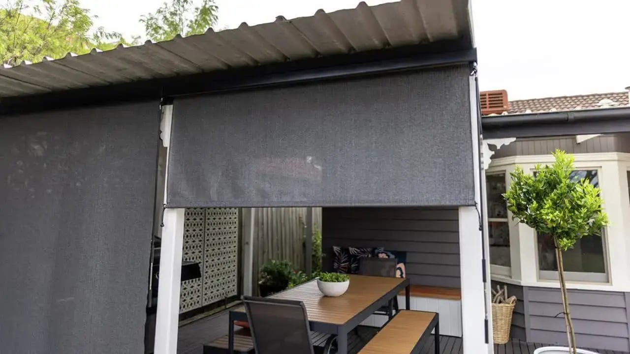 An outdoor patio area with dark roller blinds installed, showing a home improvement or trade-service instruction.