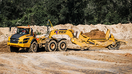 large yellow articulated dump truck towing a scraper used in the constructions industry