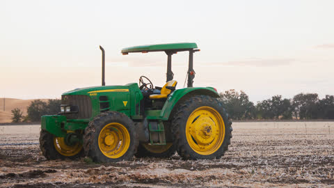 a green and yellow tractor in an agricultural field that appears to be harvested